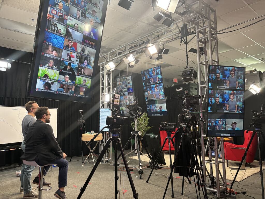 A live session in the Measurable Genius Calgary studio, with presenters, cameras, overhead lighting, and screens showing remote participants